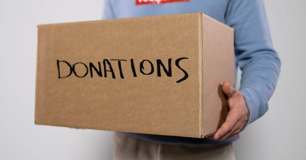 Close-up of a volunteer in a blue sweater holding a donation box. Concept of charity and volunteerism.